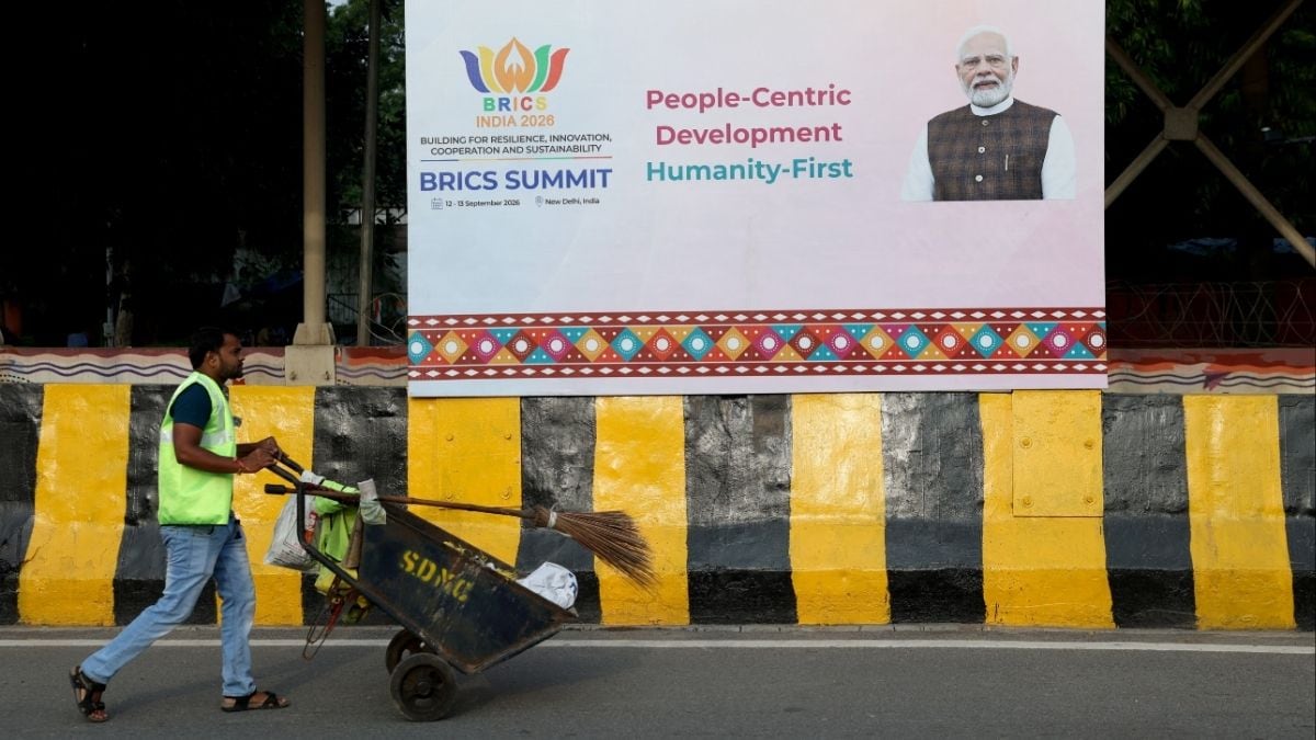 A worker pushes a cart with cleaning equipment in front of a hoarding featuring PM Narendra Modi ahead of the upcoming BRICS Summit, near Bharat Mandapam in New Delhi on September 8, 2026 | REUTERS