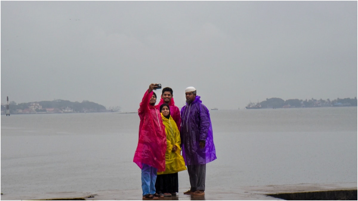 People cover themselves and click photographs during rainfall as monsoon arrives | PTI