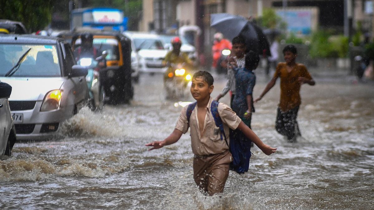 Children wade through a waterlogged area as vehicles pass by during rain, at Andheri area, in Mumbai | PTI