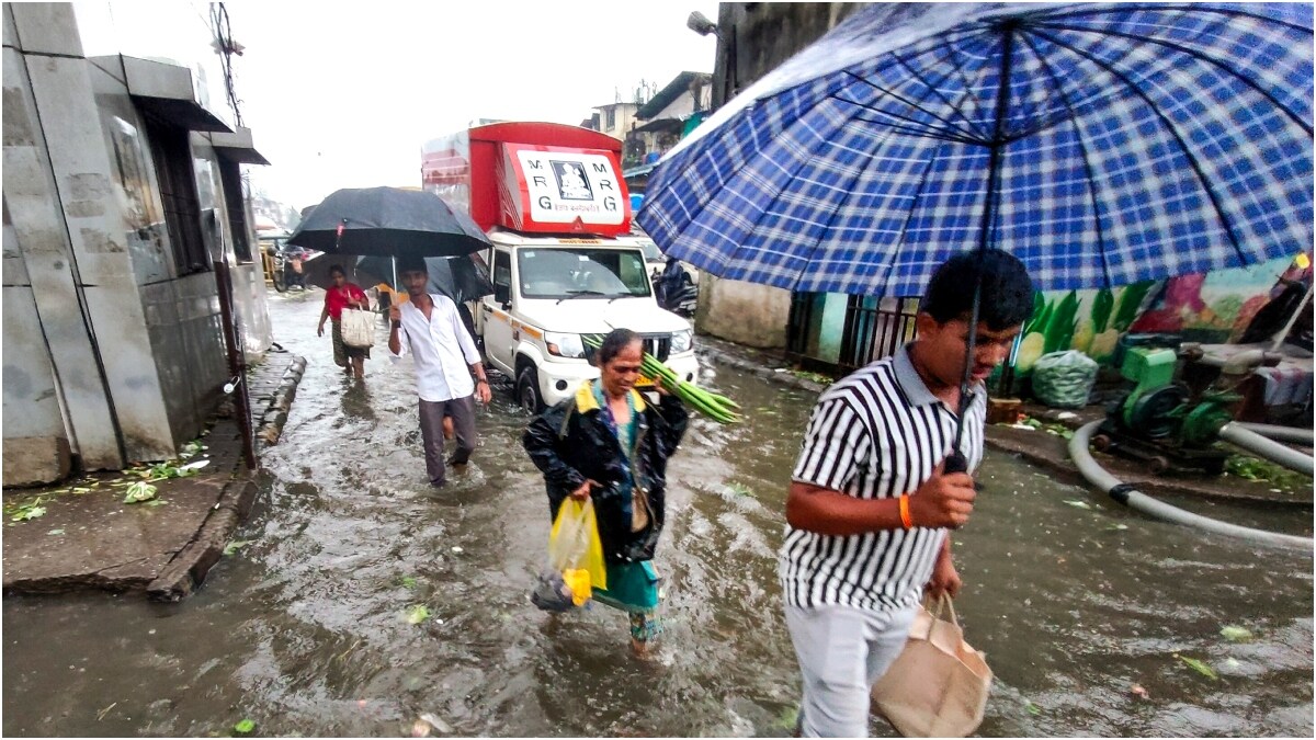 Pedestrians make their way through a waterlogged road amid rainfall, in Navi Mumbai | PTI