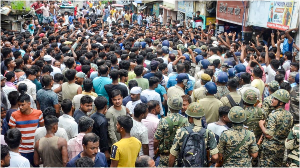 Security personnel stand guard as people block a road and stage a protest following the recovery of the body of a girl who went missing a day ago in West Bengal's Baruipur | PTI