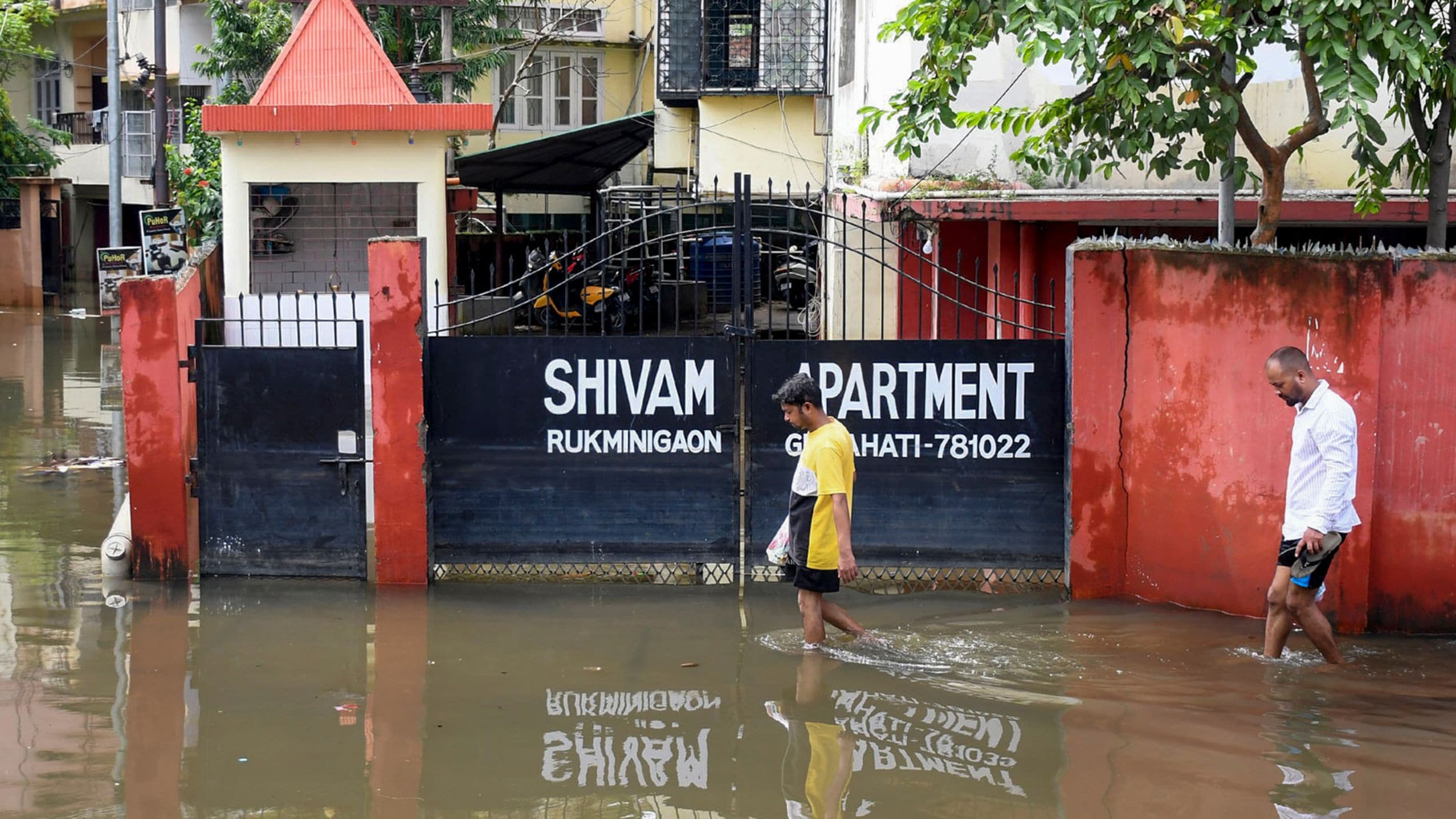 People wade through a waterlogged road at Rukminigaon after a heavy monsoon rain, in Guwahati, Assam | PTI