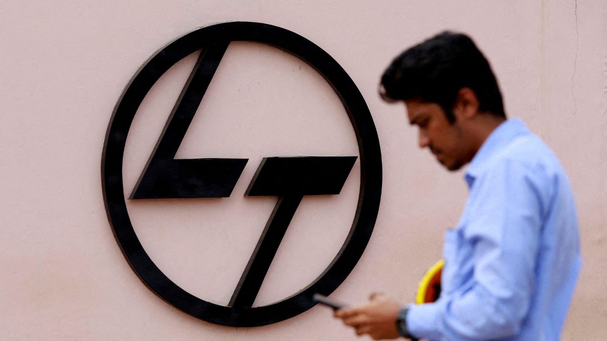 An employee checks his phone next to a logo of L&T outside the Larsen & Toubro Precision Manufacturing and Systems | Reuters
