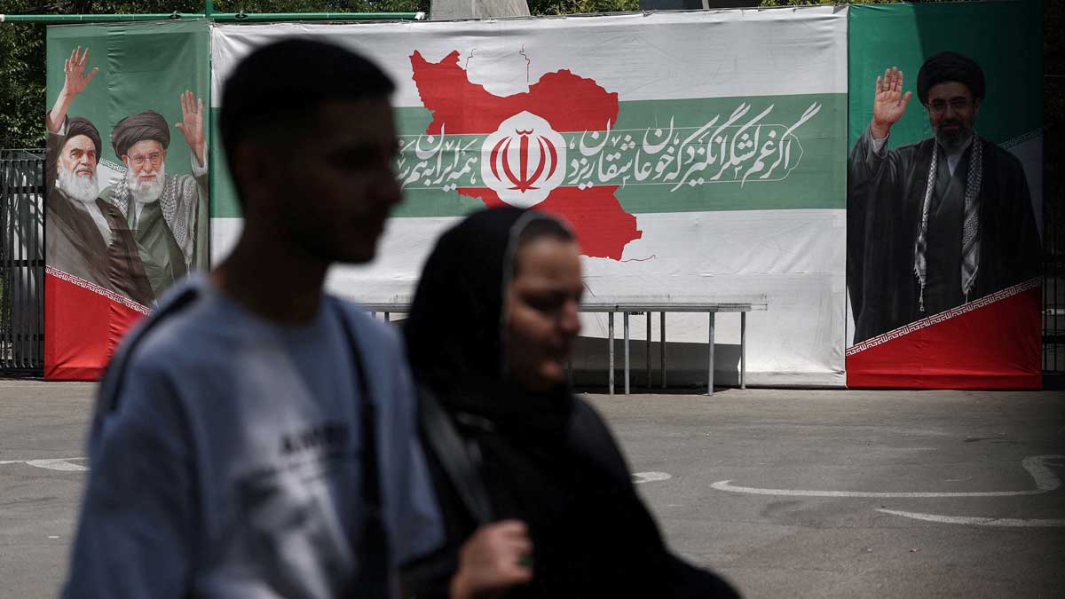 People walk past a banner with pictures of the late leader of the Islamic Revolution, Ayatollah Ruhollah Khomeini, and Iran's Supreme Leader Mojtaba Khamenei, on a street in Tehran | Reuters