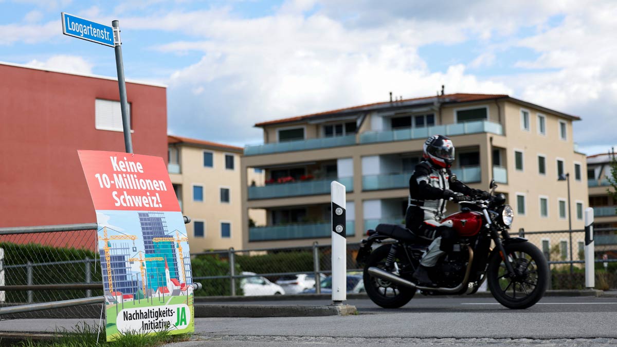 A person on a motorcycle passes a sign, on the day of the vote on a plan backed by the right-wing Swiss People's Party (SVP) to limit population growth to 10 million inhabitants, in Eichenwies, Switzerland | Reuters