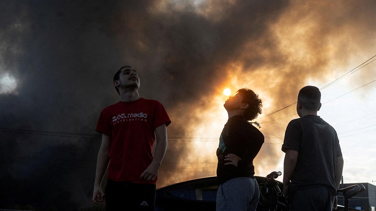 Residents look on as smoke rises over a warehouse in Kyiv, which was hit by a Russian drone | Reuters