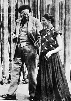 Diego Rivera and Frida Kahlo walking in front of the cactus fence at their studio house