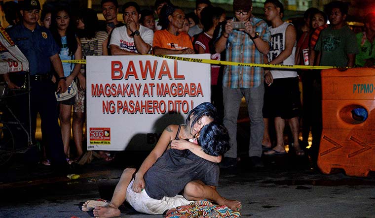 Blitz and tears: A woman in Manila hugs the body of her husband next to a sign that says “I’m a pusher”; the Duterte government has been accused of using state force to kill those it suspects of being involved in drug-related crimes | AFP