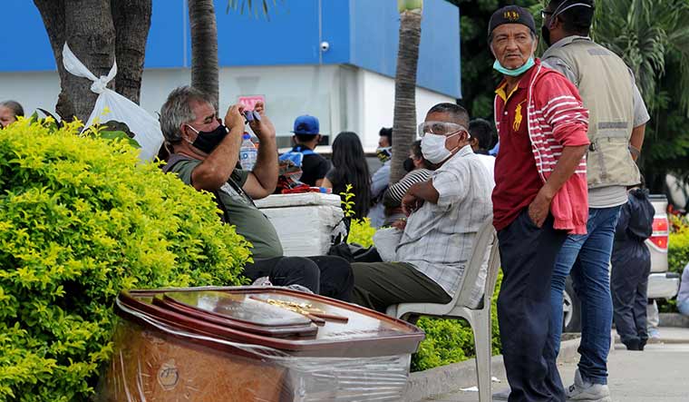 Living on the edge: Relative of a victim of Covid-19 in Guayaquil waits with a coffin for the remains | AFP