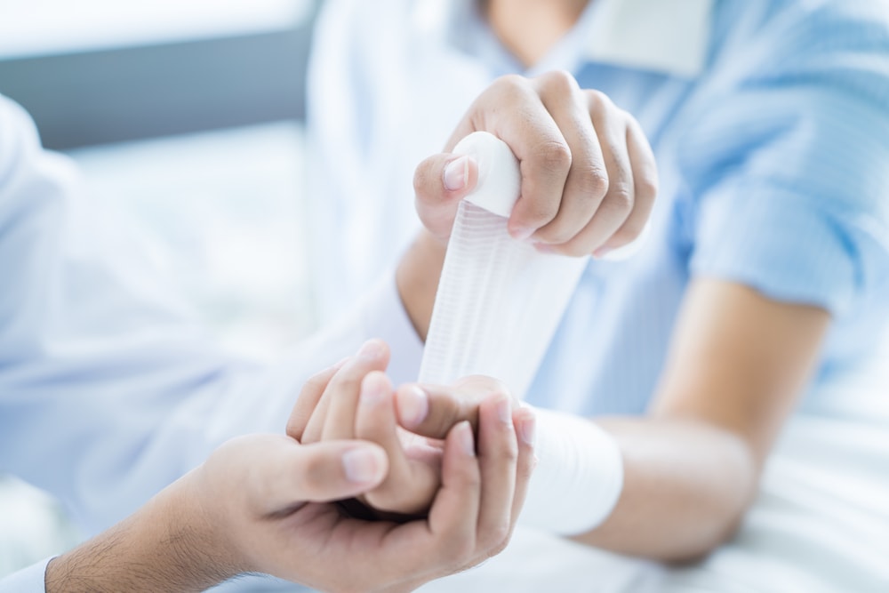 Close-up doctor is bandaging upper limb of patient.
