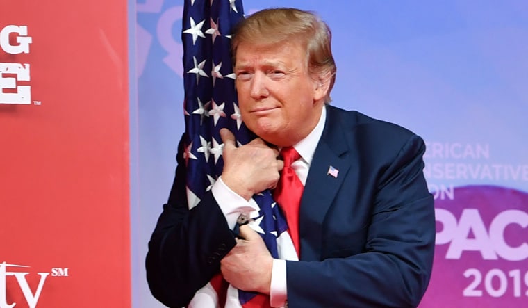 US President Donald Trump hugs the US flag as he arrives to speak at the annual Conservative Political Action Conference (CPAC) in National Harbor, Maryland, on March 2, 2019 | AFP