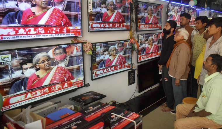 People watch Finance Minister Nirmala Sitharaman presenting Union Budget 2021-21 on television sets, at an electronics store in Prayagraj | PTI
