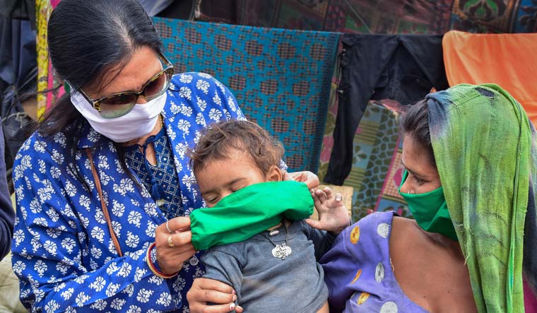A volunteer wraps a mask on a child at a slum area in the wake of deadly coronavirus, in Bikaner | PTI