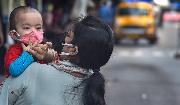A woman adjusts the protective face mask of her child, at a deserted road during the ongoing COVID-induced lockdown in Kolkata | PTI