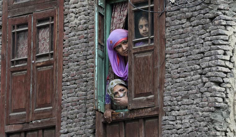 Local residents look out from a window near the site were a gun battle took place between suspected militants and security forces in Srinagar | AFP