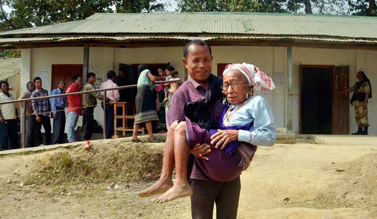 A man carries his mother after she casted her vote at a polling booth during the Tripura state assembly polls at Zaithang in Dharmanagar | PTI