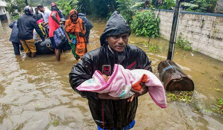 A rescuer carries an infant as people are evacuated from a flood-hit locality in Kochi | PTI