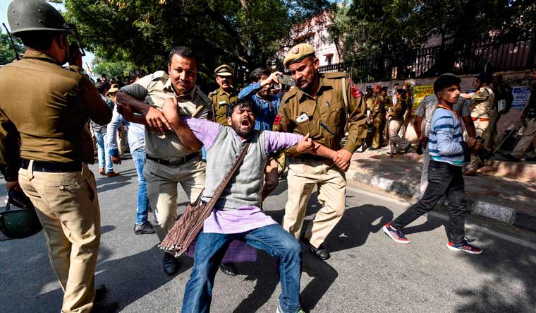 Security personnel hold a JNU student during a protest against hostel fee hike | AFP