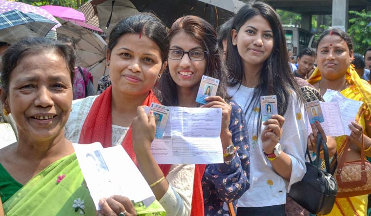 Voters show their election cards as they stand in a queue to cast their vote during the third phase of the 2019 Lok Sabha elections, at a polling station in Guwahati | PTI