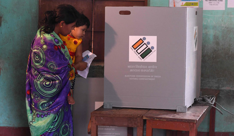A woman holds her child as she casts her vote at a polling station during the third phase of Lok Sabha elections in Guwahati | AFP