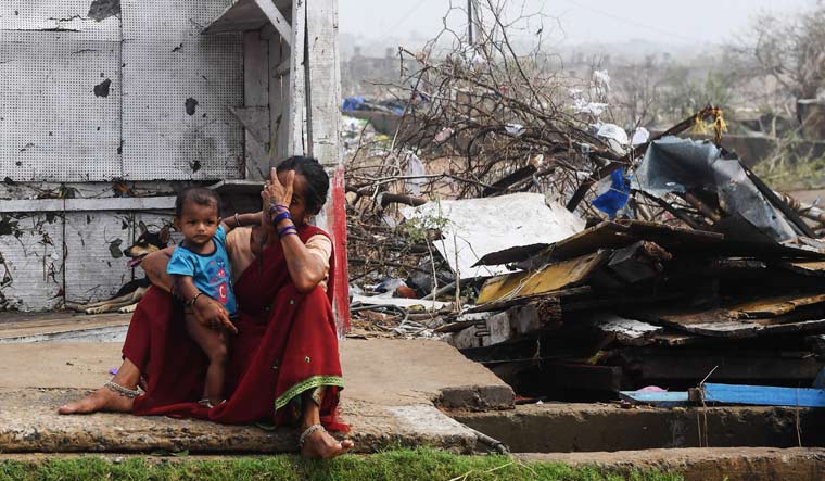 A woman sits with her child next to storm-damaged buildings in Puri in Odisha | AFP