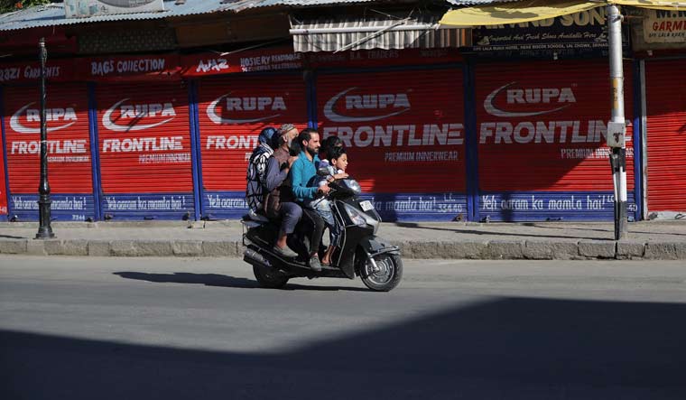 A Kashmiri family rides on a scooter past a closed market in Srinagar | AP