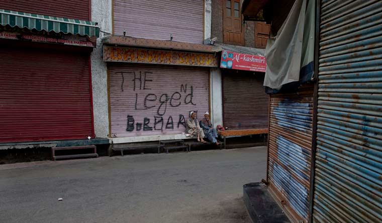 Kashmiri men sit outside a closed market in central Srinagar | AP
