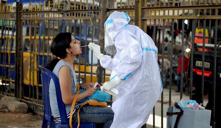 A health worker wearing a PPE kit collects sample from a woman for the COVID-19 Rapid Antigen Test, at a city market in Bengaluru | PTI