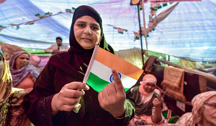 A protester, holding a tricolour, shows her ink-marked finger after casting vote for the Delhi Assembly elections, at the site of their agitation against the Citizenship Act, in Shaheen Bagh | PTI