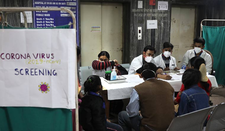Patients watch a doctor demonstrate how to cover the face while sneezing in an area set aside for possible COVID-19 cases at a free screening camp at a government run homeopathic hospital in New Delhi | AP