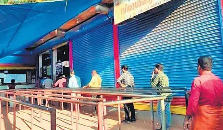 Tipplers maintain distance between one another while waiting in line at a local beverage shop in Kannur