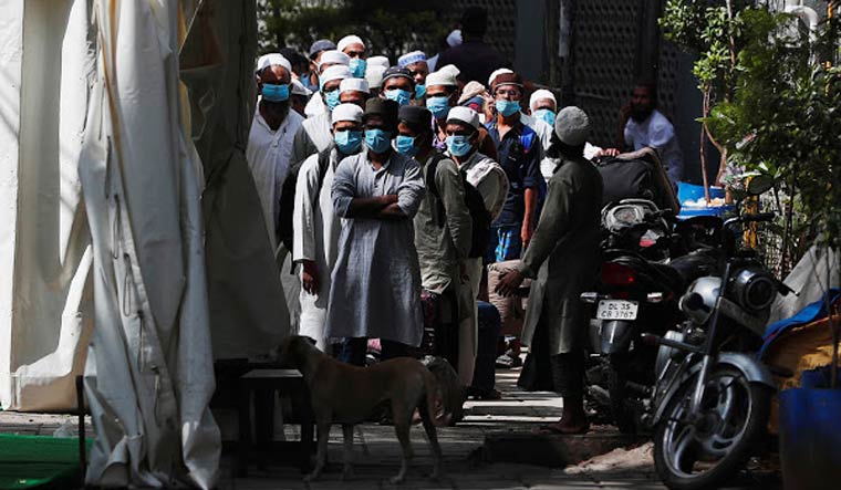 [File] Men wearing protective masks wait for a bus that will take them to a quarantine facility in Nizamuddin, Delhi | Reuters