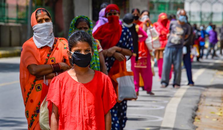 People wearing masks stand in a queue to collect food distributed by Delhi government volunteers during the ongoing coronavirus lockdown, in New Delhi | PTI