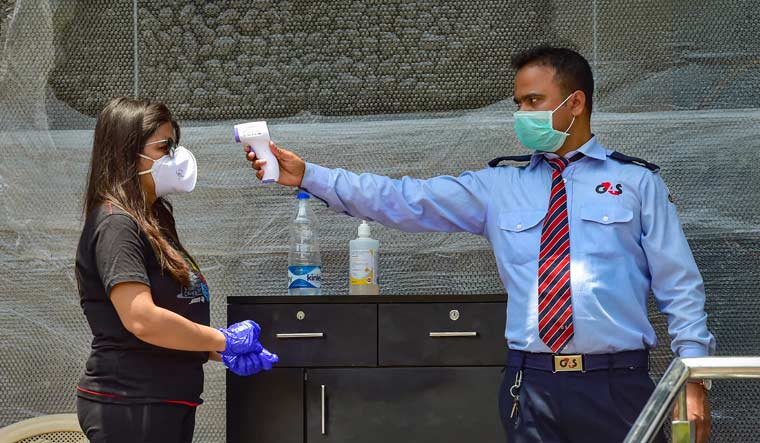 A security guard checks the temperature of a customer before allowing her to enter a liquor shop in Bengaluru | PTI