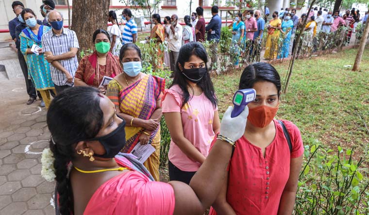 Voters undergo thermal screening as they wait in queue to cast their votes for Tamil Nadu Assembly polls, outside a polling station, in Coimbatore | PTI