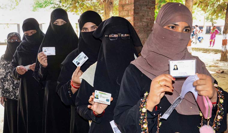 Burqa-clad women show their identification cards as they stand in a queue to cast their votes in Prayagraj | PTI