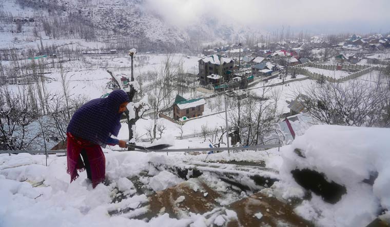 A girl clears snow from the stairs leading to her house after fresh snowfall on the outskirts of Srinagar | PTI