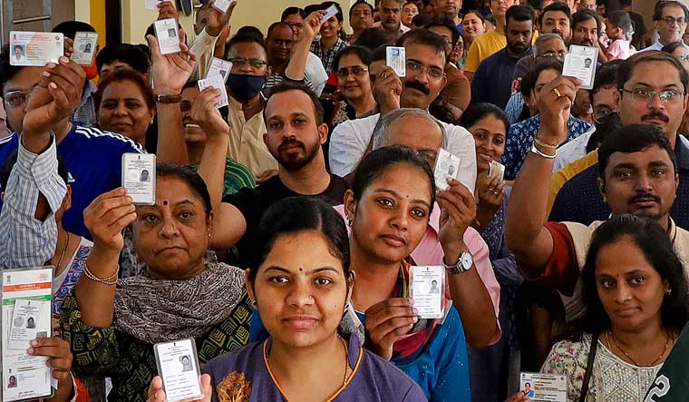 Voters pose for a photo showing their identification cards while waiting to cast their votes for the Karnataka Assembly elections, in Bengaluru | PTI