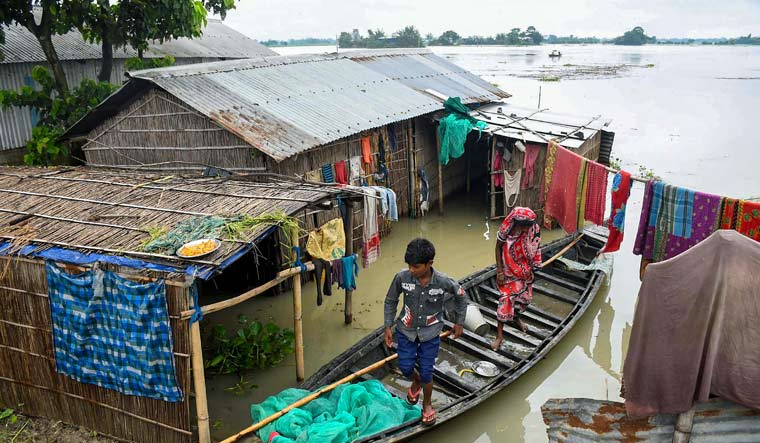 A woman and her child stand near their house submerged in flood waters at a village, in Morigaon district, Monday, June 19, 2023 | PTI