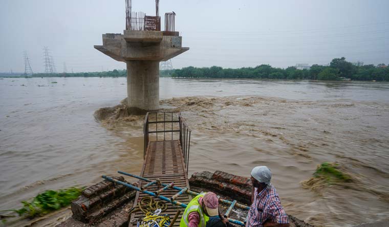 Labourers stand near an under-construction structure as the swollen Yamuna river flows in spate | PTI
