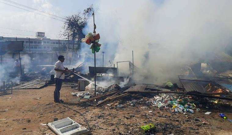 A worker sprays water to cool down burnt items at a shop which was set ablaze by miscreants in a fresh case of communal violence in Gurugram | PTI