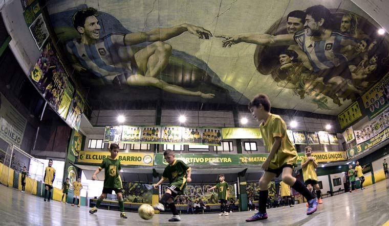 Children play indoor football at Sportivo Pereyra de Barracas football club in Buenos Aires, where local artist Santiago Barbeito created a football version of Michelangelo's "Creation of Adam"on the ceiling of the pitch | AFP