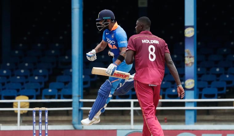 Virat Kohli jumps into the air while celebrating his century as West Indies bowler captain Jason Holder looks on during the second One-Day International cricket match in Port of Spain, Trinidad, on Sunday | AP