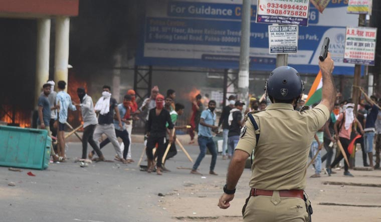 A policeman fires in the air during a protest against 'Agnipath' scheme for recruiting personnel for armed forces, in Patna, Bihar | Reuters