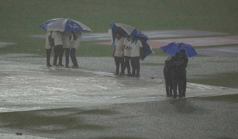 Groundsmen holding umbrellas stand near the covered pitch as it rains ahead of the IPL 2023 final cricket match between Gujarat Titans and Mumbai Indians at the Narendra Modi Stadium, in Ahmedabad | PTI