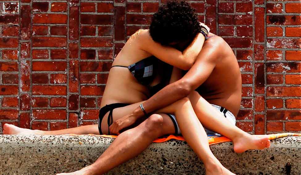 A couple embraces as another woman lies out in the sun on the steps next to the Astoria Park Pool in New York July 21, 2011. Temperatures were expected to reach near record levels Thursday as a heat wave spread east from the nation's midsection. REUTERS/Lucas Jackson (UNITED STATES - Tags: ENVIRONMENT SOCIETY) - RTR2P4TG