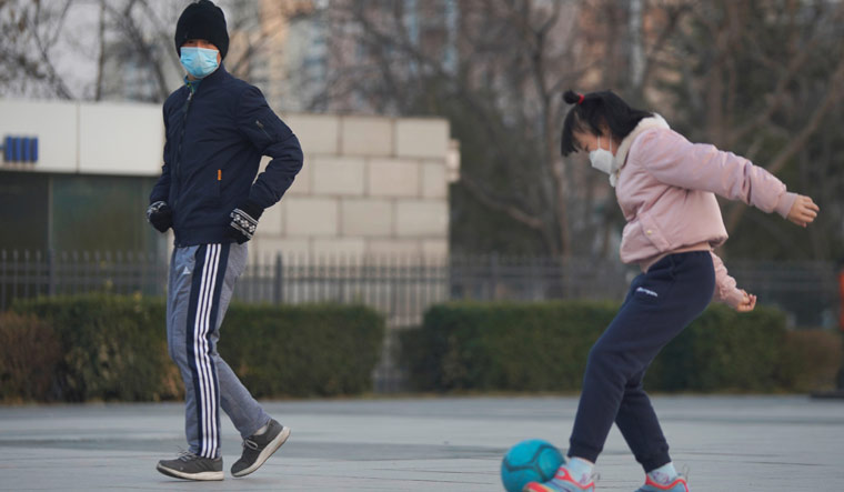 A man wearing a face mask jogs past a girl playing football at a square in Beijing, following an outbreak of the novel coronavirus in China | Reuters
