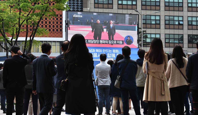 People watch live footage of South Korean President Moon Jae-in (R) walking with North Korean leader Kim Jong Un (L) at the Demilitarized Zone, on a screen in Seoul | AFP