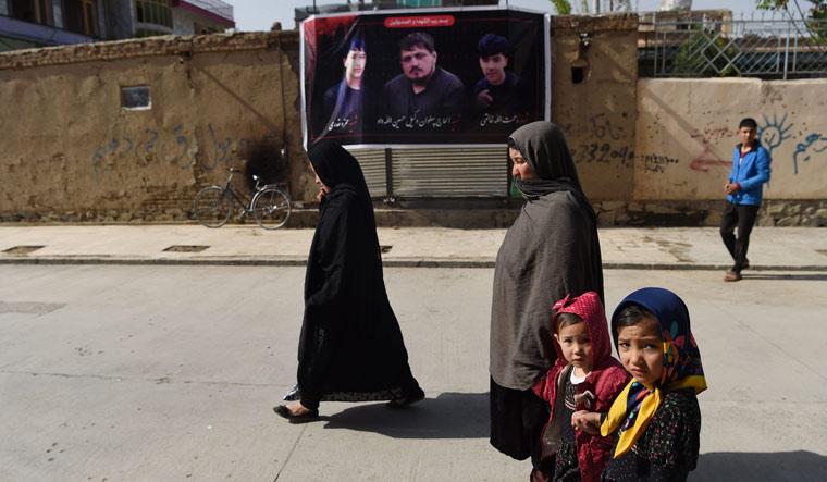 Afghan residents walk past a banner with the image of Wakil Hussain Allahdad (C), one of the 57 victims of a bomb blast, a day after the attack on a voter registration centre in Kabul on April 23 | AFP