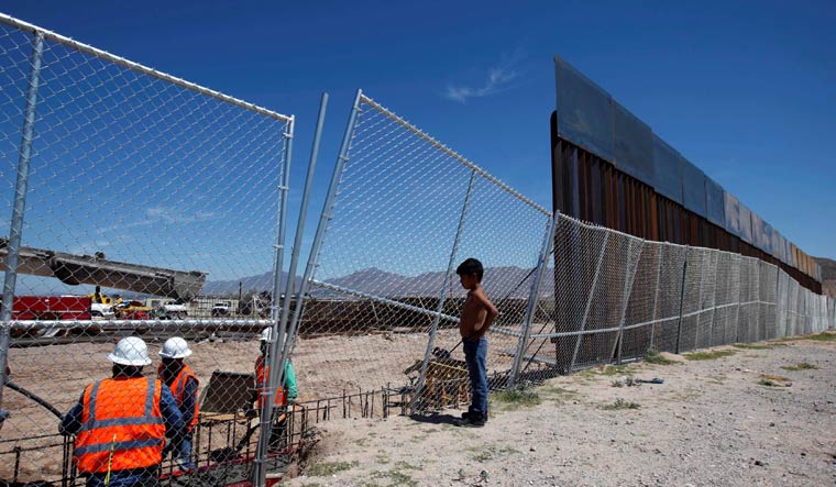 [FILE] A Mexican boy looks at US workers building a section of the US-Mexico border wall at Sunland Park, opposite the Mexican border city of Ciudad Juarez | Reuters